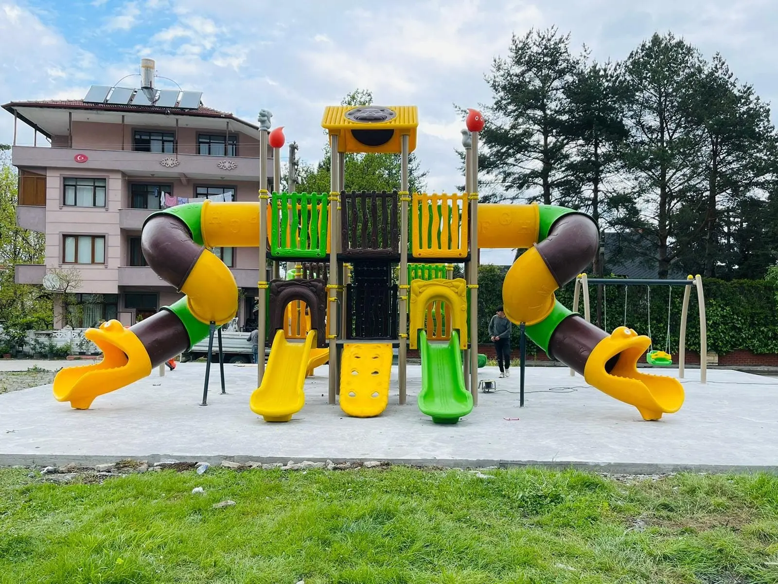 Çift tünel kaydıraklı oyun grubu ve salıncak, yeşil alan içinde