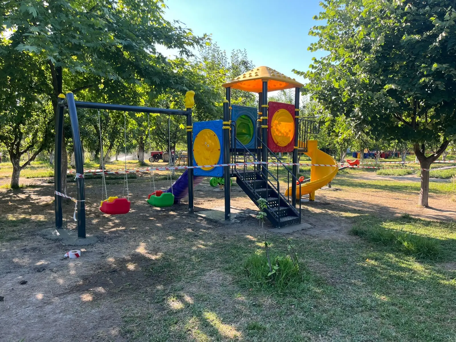 Park içinde oyun grubu ve salıncak; ağaç gölgesinde konumlandırılmış